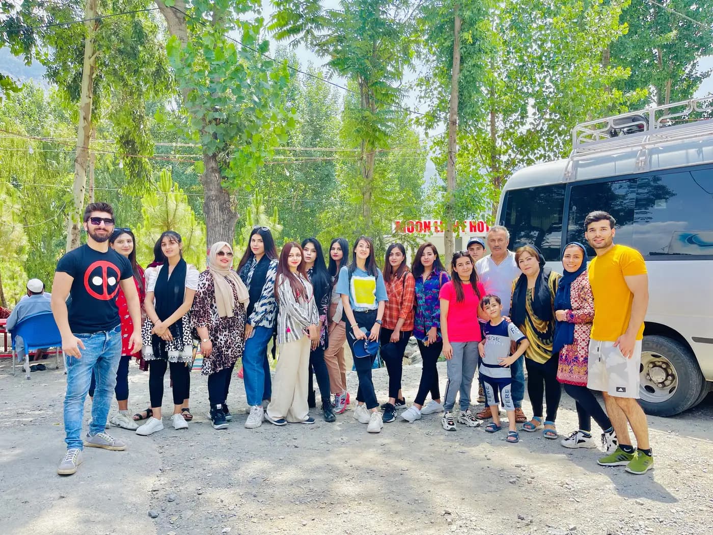 Large Lexuz Tours group standing beside their tour coaster among trees on a summer trip