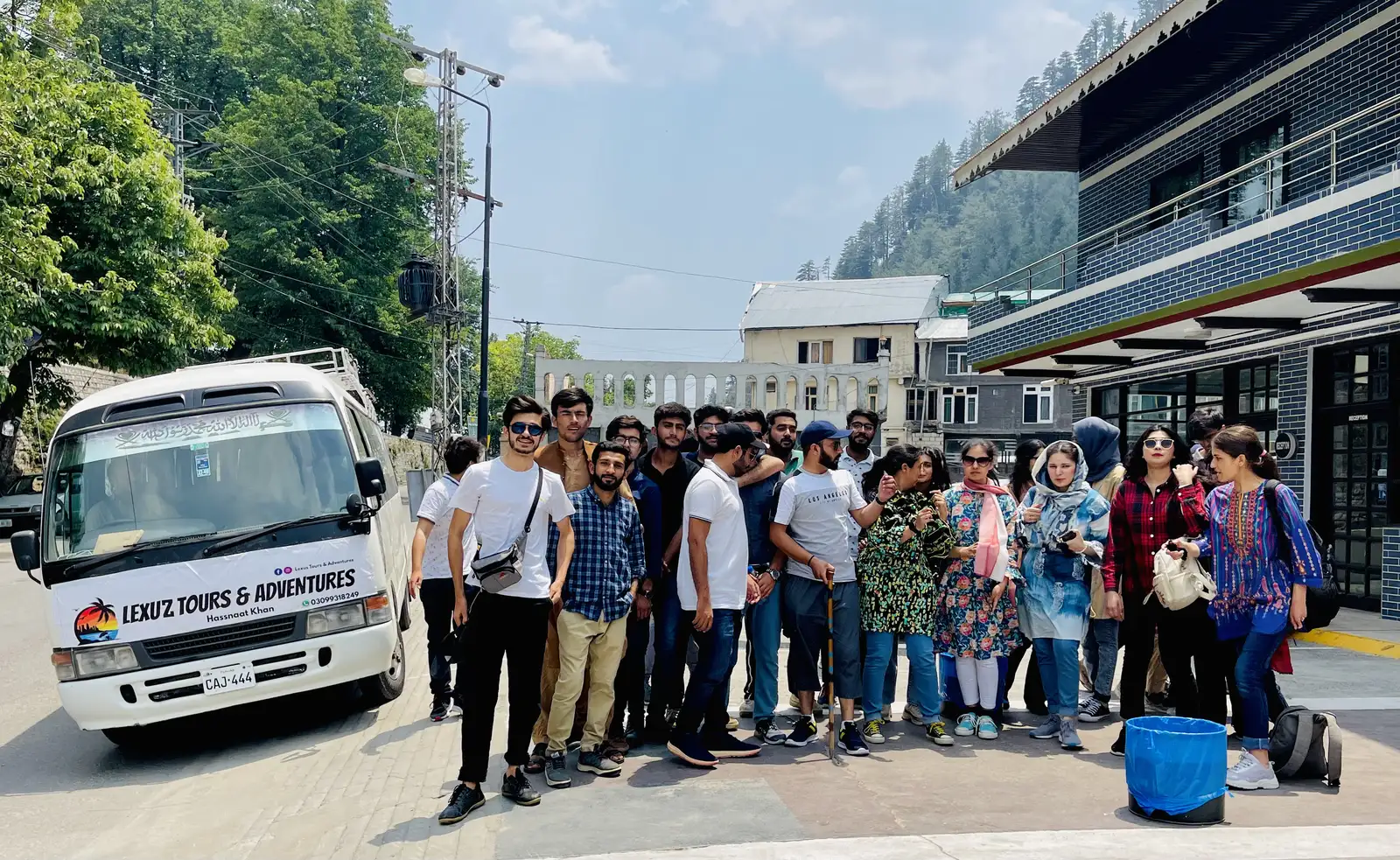 University student group in front of a Lexuz Tours & Adventures branded coaster in a hill town
